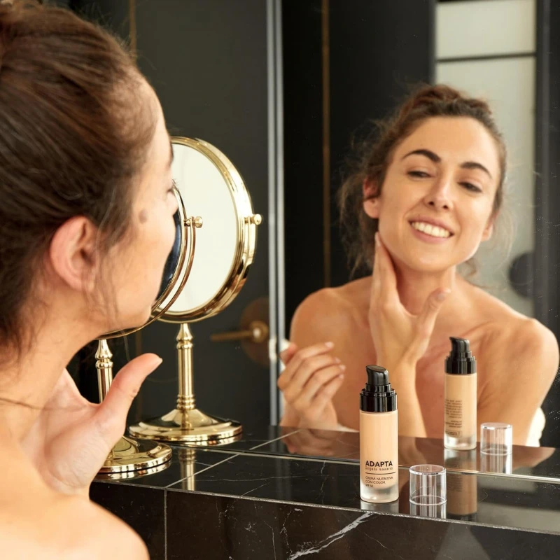 Crema Nutritiva con Color SPF50 aplicada por una mujer frente al espejo, de ADAPTA Cosmetics